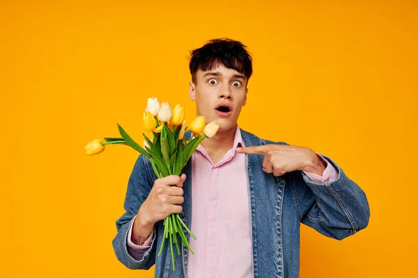 Hombre guapo con ramo de flores en chaqueta denim moda fondo amarillo — Foto de Stock