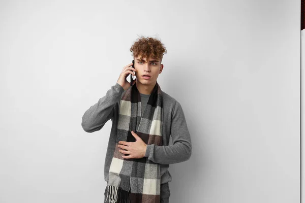Pohledný mladý muž v kostkovaném šátku při pohledu na telefon módní světlo na pozadí — Stock fotografie