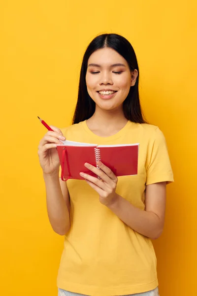एक पिवळा टी-शर्ट लाल नोटबुक प्रशिक्षण स्टुडिओ मॉडेल मध्ये आकर्षक तरुण आशियाई स्त्री अनियंत्रित — स्टॉक फोटो, इमेज