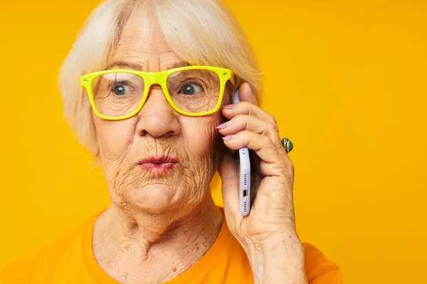 Sarı gözlüklü yaşlı bir kadın telefonda konuşuyor. — Stok fotoğraf