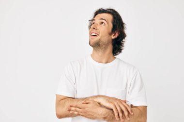 Beyaz tişörtlü bir adam. El hareketi. Arka plan hafif.