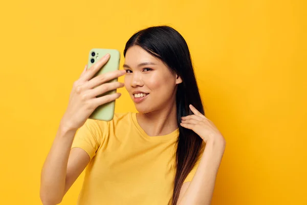 Pretty brunette with a phone in her hands makes a selfie yellow background unaltered — Foto Stock