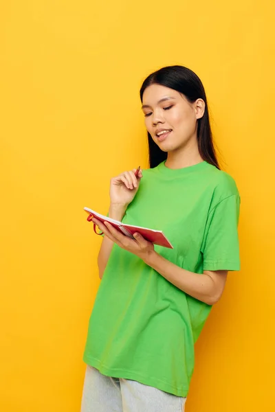 Femme avec apparence asiatique T-shirts verts avec carnet rouge et stylo fond jaune inchangé — Photo