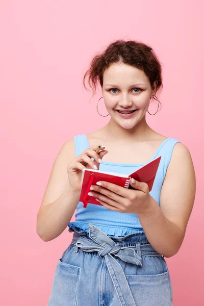 Belle femme écrivant dans un carnet rouge avec un stylo étude couleur rose fond inchangé — Photo