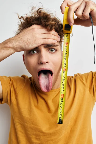 Pohledný mladý muž měření páska opatření ve žluté t-shirt světlo pozadí — Stock fotografie