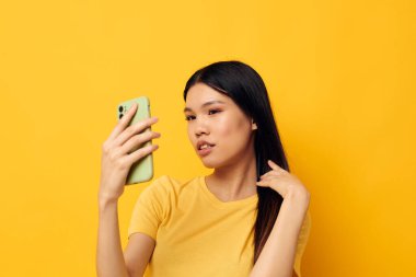 Sarı tişörtlü Asyalı güzel bir kadın telefona bakıyor. Yaşam tarzını değiştirmeden poz veriyor.