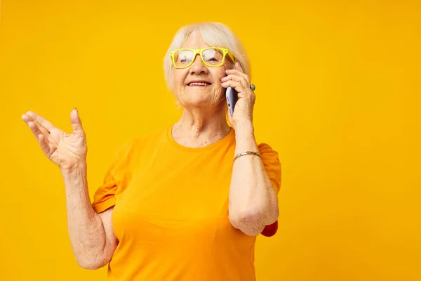 Gülümseyen yaşlı kadın mutlu bir yaşam tarzı. Sarı tişörtler ve telefon yakın çekim duyguları. — Stok fotoğraf