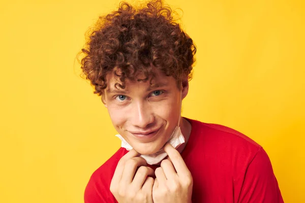 Kerl mit roten lockigen Haaren in einem roten T-Shirt medizinische Maske Schutz gelb Hintergrund unverändert — Stockfoto