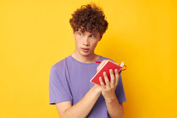 Young curly-haired man notepad with pen learning emotions yellow background unaltered — Stock fotografie