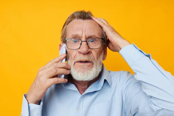 Portrét starší muž šedé vousy s brýlemi mluvit na žlutém pozadí telefonu — Stock fotografie