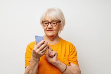 Tişört giyen, güneş gözlüklü yaşlı bir kadın telefon ışığı arka planında konuşuyor.
