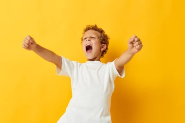 Beyaz tişörtlü neşeli çocuk stüdyo sarısı arka planda poz veriyor.