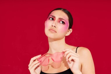 Genç ve güzel bir kadın pembe gözlüklü parlak makyajlı siyah formalı pembe arka planı değiştirilmemiş.