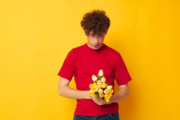 Retrato de un joven rizado romántico posando con un ramo amarillo de flores fondo amarillo inalterado — Foto de Stock