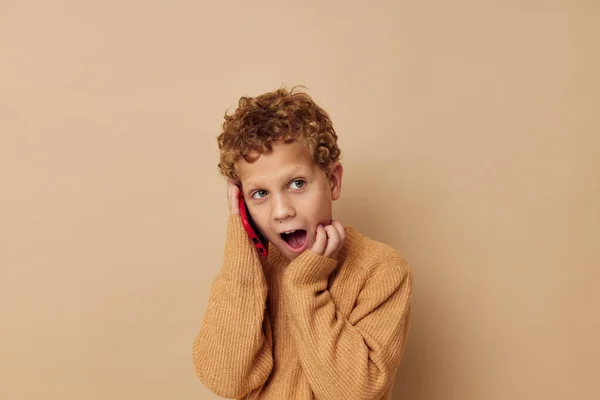 Курчавый мальчик разговаривает по телефону, позируя бежевый фон — стоковое фото