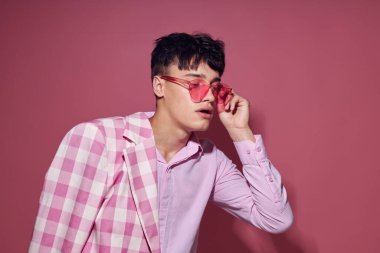 Pembe gözlüklü genç bir adam. Pembe ceketli. Stüdyo pembe arka planda.