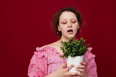 Çekici genç bir kadın ayakta ve saksıda çiçek tutuyor.