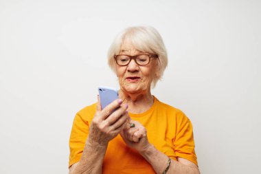 Sarı tişörtlü gülümseyen yaşlı kadın telefonla iletişim kuruyor.