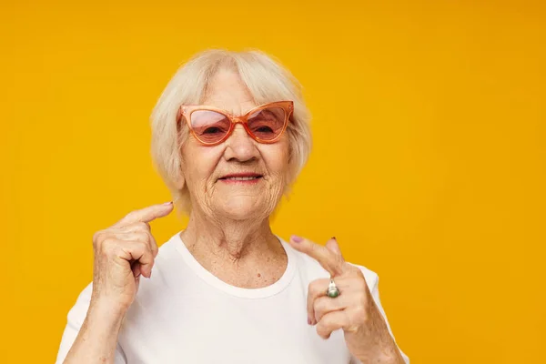 Mujer anciana sonriente en una camiseta blanca lleva gafas de fondo aislado — Foto de Stock