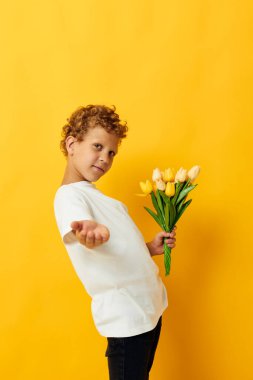 Çiçek buketi olan beyaz tişörtlü küçük bir çocuk. Stüdyonun izole edilmiş bir arka planı var.