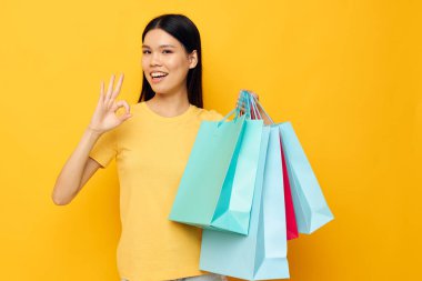 Sarı tişörtlü, çok renkli alışveriş çantalı, Asyalı güzel kadın portresi. Stüdyo modeli değiştirilmemiş.