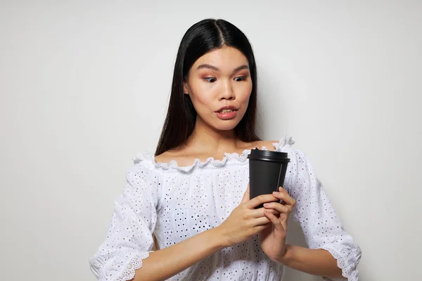 Tek kullanımlık bir bardak içecekle poz veren Asyalı güzel bir genç kadın portresi değiştirilmemiş bir arka plan. — Stok fotoğraf