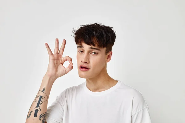 Porträtt av en ung man tatuering på händer i vit t-shirt ljus bakgrund oförändrad — Stockfoto