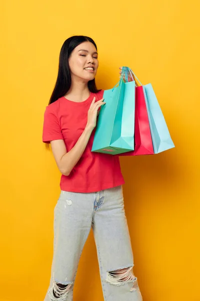 Charmante jonge Aziatische vrouw met veelkleurige boodschappentassen gele achtergrond ongewijzigd — Stockfoto
