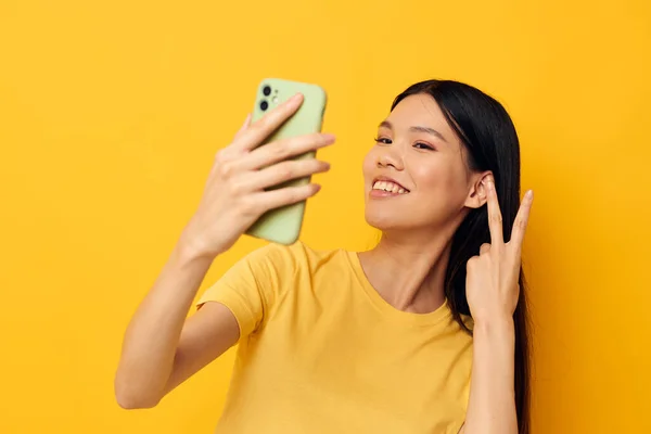노란 티셔츠를 입고 변경되지 않은 생활 방식을 보여 주는 전화를 보고 있는 아시아의 아름다운 여성 — 스톡 사진