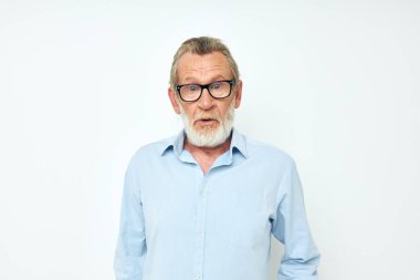 Kıdemli, gri saçlı, mavi tişörtlü adam el hareketleriyle arka planını aydınlatıyor.