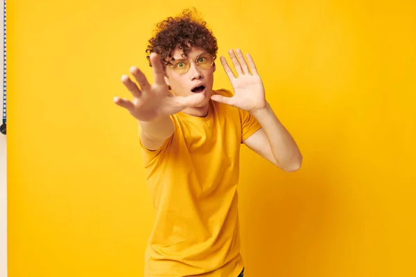 Genç kıvırcık saçlı adam sarı t-shirt gözlükleri moda el hareketleri sarı arka plan değiştirilmemiş — Stok fotoğraf