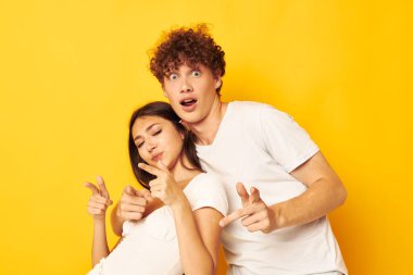 Genç adam ve kız beyaz tişörtler içinde birlikte poz veriyorlar. Dostluk sarı arka plan değiştirilmemiş.