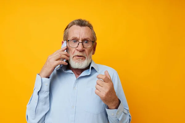 Hombre de pelo gris senior con una camisa azul y gafas hablando en el fondo aislado del teléfono —  Fotos de Stock