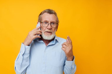 Telefon sapsarı arka planda konuşan gözlüklü yaşlı bir adam portresi.