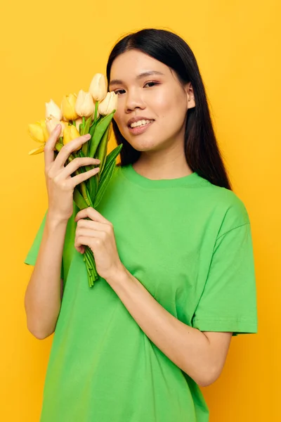 Mulher t-shirt verde um buquê de flores amarelas fundo amarelo inalterado — Fotografia de Stock