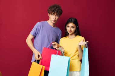 Renkli tişörtleri olan genç bir çocuk ve kız çantalarla alışveriş yapıyorlar. Yaşam tarzlarını değiştirmiyorlar.