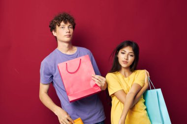 Renkli tişörtleri olan genç bir çocuk ve kız çantalarla alışveriş yapıyorlar. Yaşam tarzlarını değiştirmiyorlar.