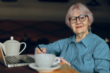 Dizüstü bilgisayarın önünde çalışan yaşlı bir kadın oturmuş, değişmeden sohbet ediyor.