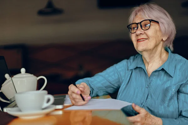 Anciana sentada en un café con una taza de café y una laptop Lifestyle inalterada — Foto de Stock