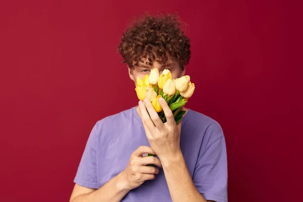 Un joven sosteniendo un ramo amarillo de flores camisetas púrpuras fondo rojo inalterado — Foto de Stock