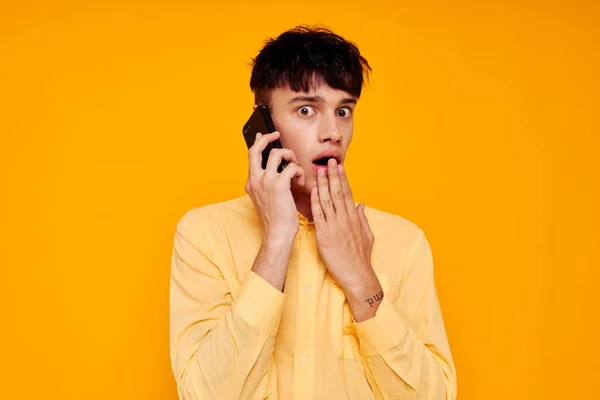 Młody facet w żółtej koszuli mówi przez telefon odizolowane tło — Zdjęcie stockowe