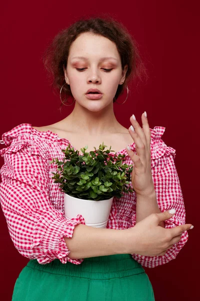 Ayakta duran ve saksıda çiçek tutan genç bir kadın. Kırmızı arka plan değiştirilmemiş.