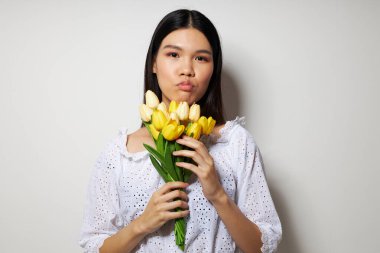 Çiçek buketi olan bir kadın gülüyor. Arka planda hiç değişmemiş bir ışık var.