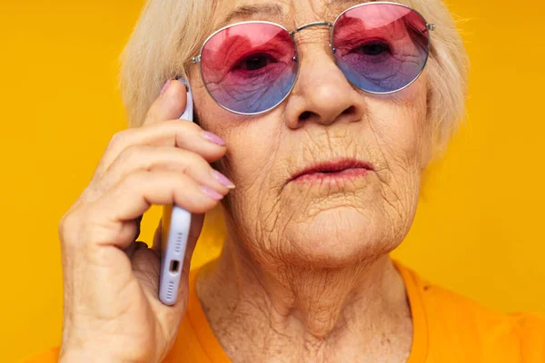 Пожилая женщина разговаривает по телефону в желтых очках желтый фон — стоковое фото