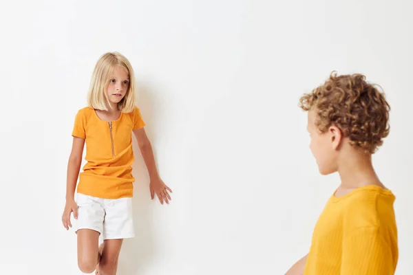 Мальчик и девочка в желтых футболках стоят рядом друг с другом на светлом фоне, позируя — стоковое фото