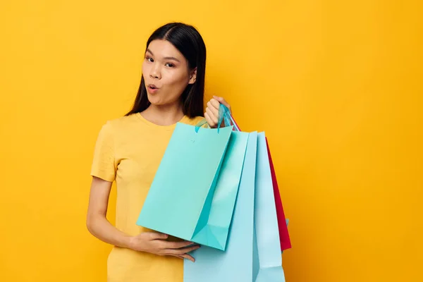 Portret Aziatische mooie jonge vrouw in een geel T-shirt met veelkleurige boodschappentassen studio model ongewijzigd — Stockfoto