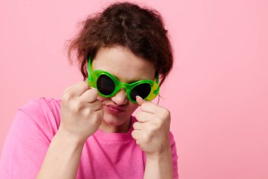 Pembe tişörtlü, yeşil gözlüklü güzel bir kadın. Gençlik modası, pembe arka plan.
