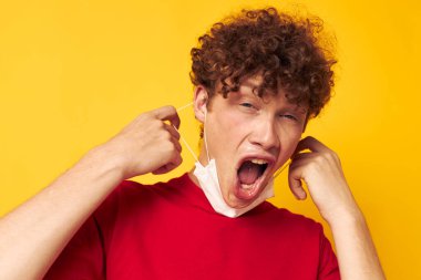 Kırmızı tişörtlü, kıvırcık saçlı genç adam yüzüne tıbbi bir maske takıyor.