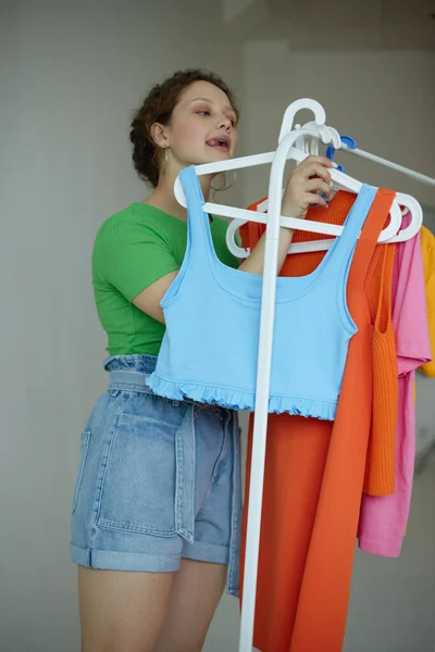 Retrato de una mujer joven planchando ropa sobre un fondo de luz armario percha inalterado —  Fotos de Stock