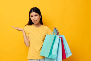 Sarı tişörtlü, Asyalı bir kadın. Çok renkli alışveriş çantalı. Stüdyo modeli değiştirilmemiş.